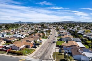 Aerial view of a suburban neighborhood with single-family homes, residential streets, and rolling hills under a blue sky.