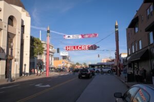 Hillcrest neighborhood entrance sign spanning a busy street with pedestrians, vehicles, and commercial buildings in San Diego.