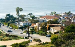 Coastal neighborhood with homes, palm trees, and ocean views along a scenic residential street near the shoreline.